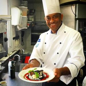 a chef holding a plate of food in a kitchen at Lummina Barueri Alphaville in Barueri