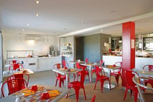 a restaurant with tables and red chairs and a kitchen at Hotel Funtana Marina in LʼÎle-Rousse