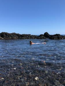 a person swimming in the water near a rocky beach at A Villa by the Sea Bed & Breakfast in Vila Franca do Campo