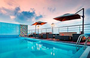 a swimming pool with two umbrellas and chairs and a pool at Zone By The Park, ORR, Chennai in Chennai