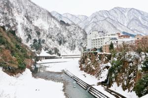 a river with snow on the side of a mountain at Entaijiso in Kurobe