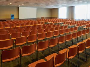 una sala conferenze vuota con sedie arancioni e schermo di Novotel Rio de Janeiro Parque Olimpico a Rio de Janeiro