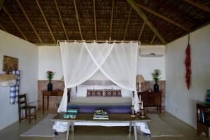 a bedroom with a bed with a curtain and a table at Le Paxa Casa Hotel & Spa in Caraíva