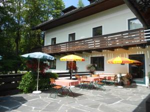 un patio con tavoli e ombrelloni di fronte a un edificio di Pension Wanderruh a Grünau im Almtal