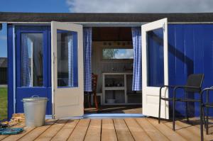 eine offene Tür zu einem blauen Haus mit einer Terrasse in der Unterkunft Sitting at the Bay in Zuiderwoude
