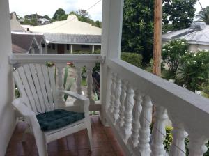 a white rocking chair on a balcony with a view at Coconut cottage in Bridgetown