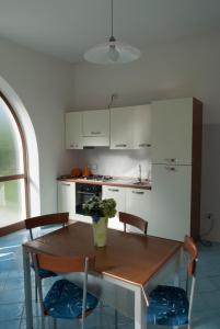 una cocina con mesa de madera con sillas y una cocina con armarios blancos. en L'Approdo di Giasone, en Foce del Sele