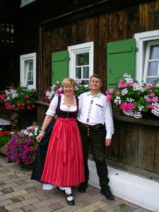 a man and a woman standing in front of a building with flowers at Schusterhof in Mittelberg