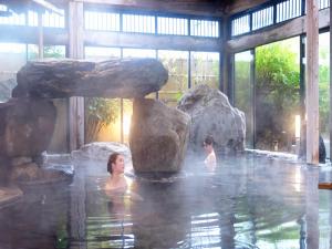 two women in a pool of water with rocks at Yuraku Hotel in Awara