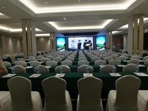 una habitación con sillas y una pantalla con 2 personas en un escenario en Wudang International Hotel en Shiyan