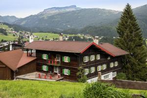 a large wooden house with green windows and a mountain at Gästehaus Walserheimat in Riezlern