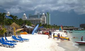 un grupo de personas en una playa con sillas y agua en Sandcastle Beach Apartments, en Palm-Eagle Beach