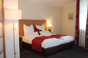 une chambre d'hôtel avec un lit et une couverture rouge dans l'établissement Ambassador Hotel, à Grasbrunn
