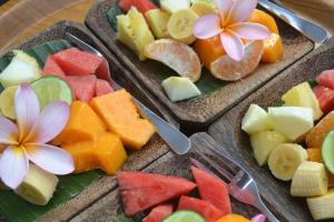 three plates of fruit on a table with utensils at Suka's House Bed & Breakfast in Ubud