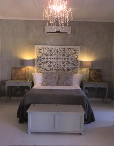 1 dormitorio con 1 cama con lámpara de araña y 2 mesas en GABRIELLA'S, en Riebeek-Kasteel
