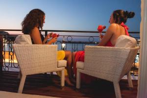 卡尼亞鎮的住宿－Domus Fresco，两个女人坐在阳台上的椅子上,阳台上有玫瑰