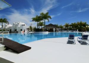 una gran piscina con 2 sillas y palmeras en BLU PARADISE COSTA ADEJE - Heated Pool, en Adeje