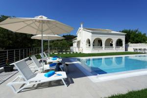 una piscina con sillas, una sombrilla y una casa en Villa Vozos en Arillas