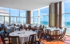 a dining room with tables and chairs and windows at TRYP by Wyndham Lisboa Caparica Mar in Costa da Caparica