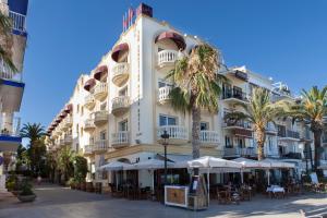 a large white building with tables and umbrellas at URH Sitges Playa in Sitges