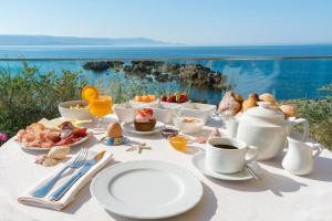 a table with breakfast food and coffee on a table with the ocean at Hotel Dei Pini in Alghero