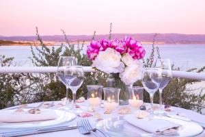 a table with glasses and a vase of pink flowers at Hotel Dei Pini in Alghero