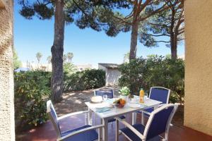 une table et des chaises blanches sur un patio arboré dans l'établissement Résidence Odalys Saint Loup, au Cap d'Agde