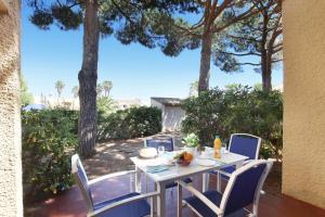 a white table and chairs on a patio with trees at Résidence Odalys Saint Loup in Cap d'Agde