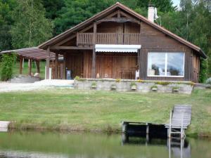 uma casa de madeira com uma cadeira em frente a um lago em Lieux-au-lac em Augignac