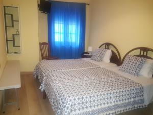 1 dormitorio con 2 camas y una ventana con cortinas azules en Caldeira Guest House, en Oporto