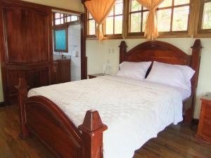1 dormitorio con cama de madera, sábanas blancas y ventanas en Paysage Cache, en Estelí