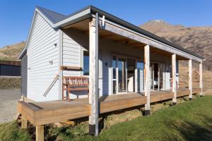 uma pequena casa branca com um alpendre em madeira em Shotover Country Cottages em Queenstown