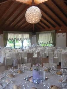 Großes Zimmer mit weißen Tischen, Stühlen und einem Kronleuchter. in der Unterkunft Hotel Centro Benessere Gardel in Arta Terme