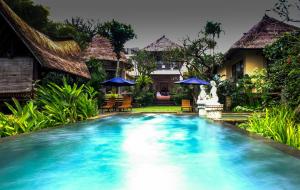 a pool in front of a house with chairs and umbrellas at Villa Sebali in Ubud