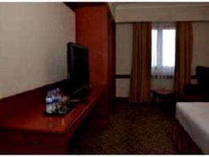 a hotel room with a bed and a desk with a television at Abadi Suite Hotel & Tower in Jambi