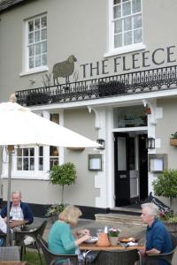 eine Gruppe von Personen, die vor einem Gebäude an Tischen sitzen in der Unterkunft The Fleece in Witney