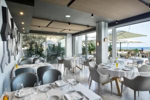 um restaurante com mesas e cadeiras brancas e janelas em Hotel Boutique dONNA 4* Superior em Castelldefels