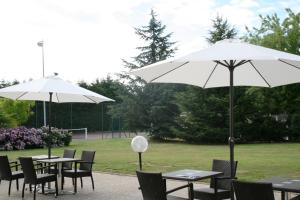dwa stoły i krzesła z parasolami w parku w obiekcie Escale Oceania Nantes Aéroport w mieście Bouguenais