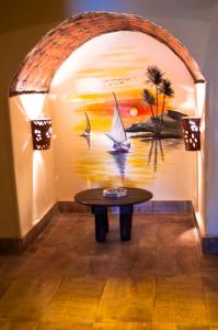a table in a room with a painting of a sailboat at Hadouta Masreya Nubian Guest House in Aswan