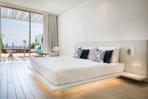 a white bedroom with a large bed and a balcony at Mykonos Dove Beachfront Hotel in Platis Gialos