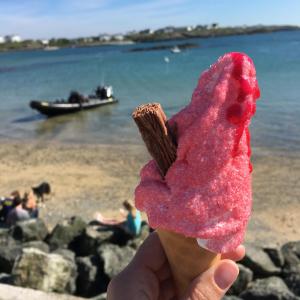 a person holding a pink treat with a beach in the background at The Beach Motel in Trearddur