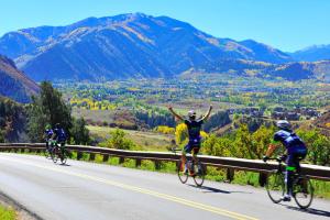 three people riding bikes down a road with their arms in the air at The Little Nell in Aspen