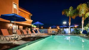 a swimming pool with chairs and umbrellas at night at Best Western Plus Diamond Valley Inn in Hemet
