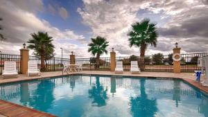 a swimming pool with chairs and a fence and palm trees at Best Western Bastrop Pines Inn in Bastrop