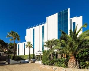 a tall white building with palm trees in front of it at Boutique Hotel H10 Blue Mar - Adults Only in Camp de Mar