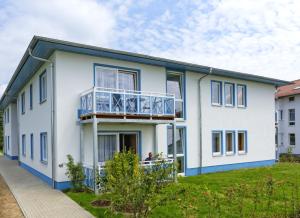 uma casa branca com acabamento azul e uma varanda em Appartementhäuser Achterwasserblick em Ostseebad Koserow