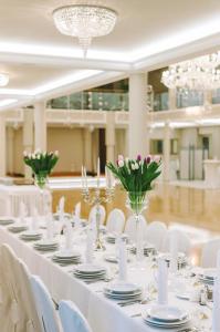 une grande table avec des chaises blanches et des vases avec des fleurs dans l'établissement Hotel i Restauracja Jan, à Bełchatów