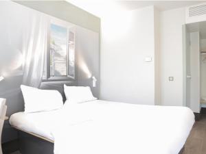 a white bedroom with a large bed and a window at B&B HOTEL Hyeres in Hyères