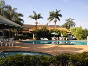 a pool with chairs and tables and palm trees at Rio Claro Plaza Hotel in Rio Claro