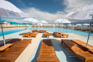 a swimming pool with wooden benches and white umbrellas at Aquamarine Resort in Akshi